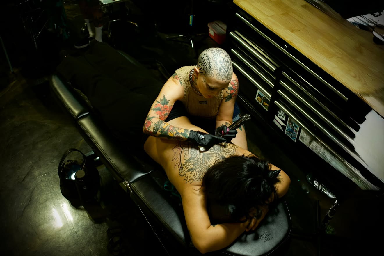 Overhead view of Jenna tattooing a large ornamental back piece on a client lying on the studio chair